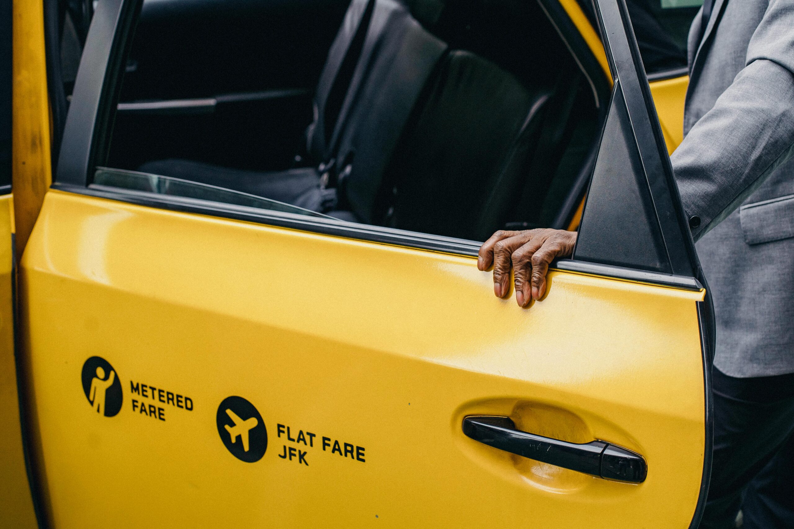 A person opens a yellow taxi door with JFK flat fare signage.